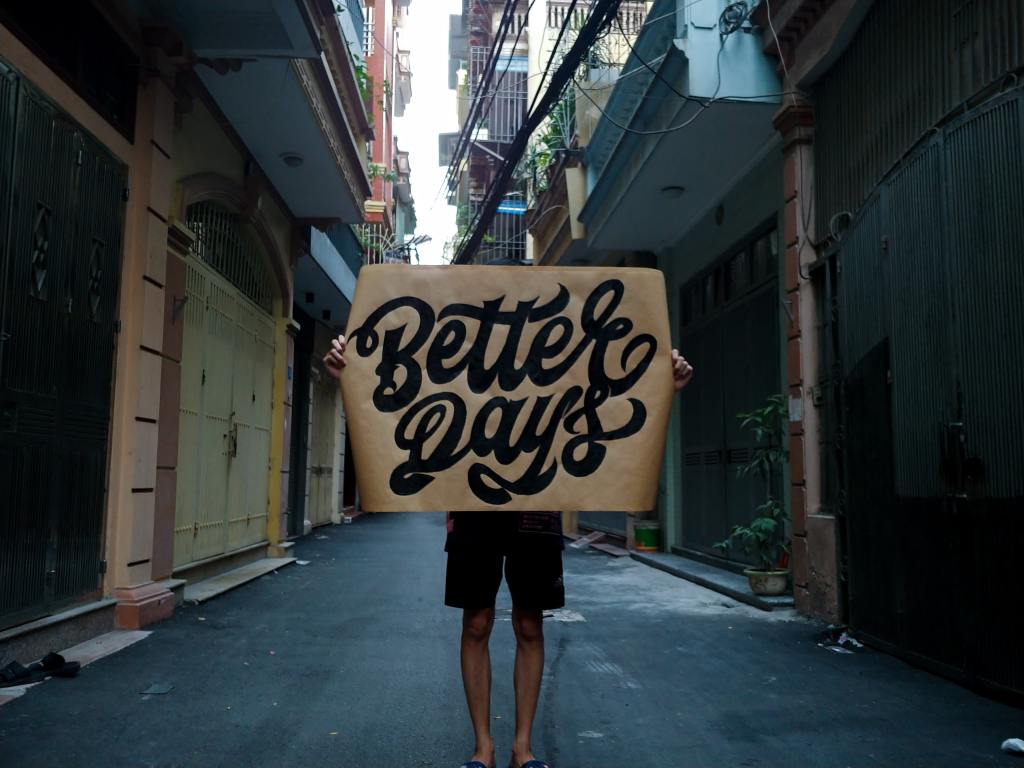A stock image of a person standing in the middle of a street holding a sign that says 'Better Days'.