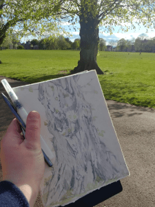 The photographer holds their journal up in front of the camera with a drawing of the tree in the distance on the journal page.