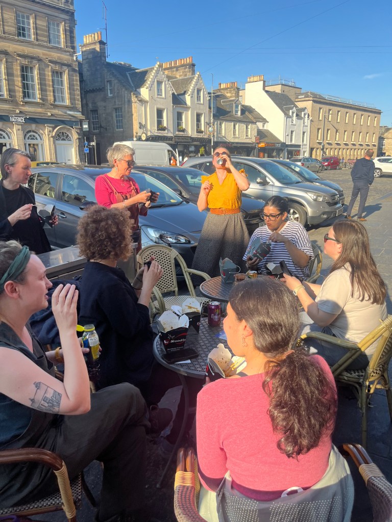 A group of friends standing or sitting at bistro tables outside on the pavement