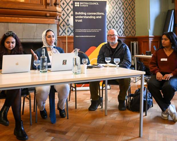 Four people seated at a table during a panel discussion, with laptops, water glasses, and a British Council Scotland banner in the background.