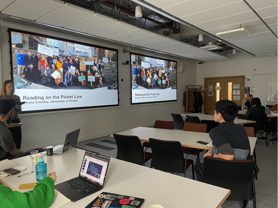 Keynote session at the University of Glasgow with attendees seated in a seminar room while a presentation slide titled “Reading on the Picket Line” is displayed.