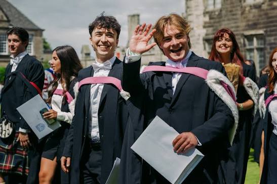 Two male graduates of the University of St Andrews in Scotland smile for the camera as they celebrate.