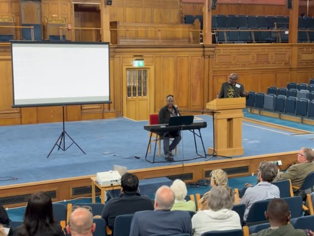Professor Jean Kidula sitting at her keyboard singing during her presentation at the conference.